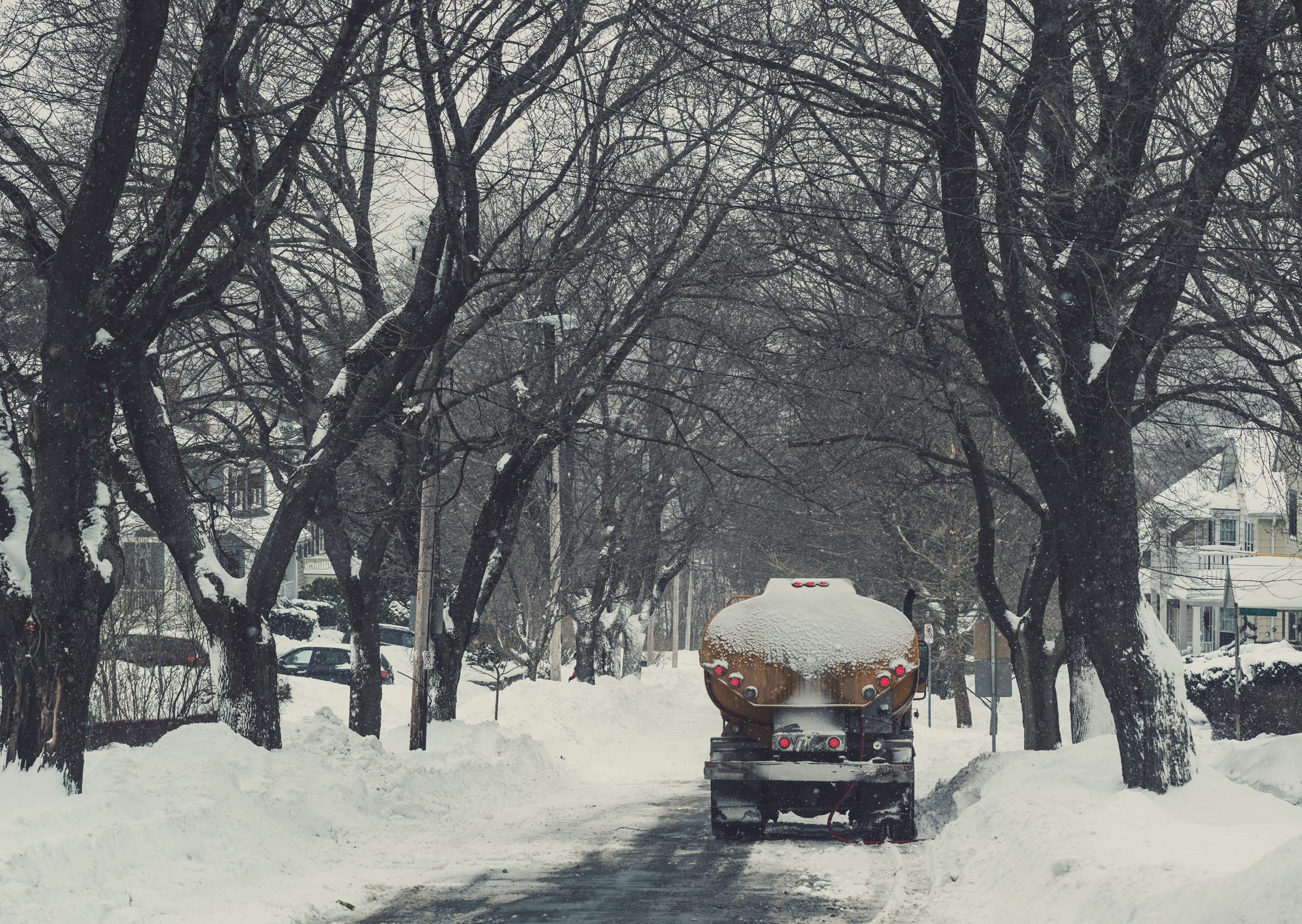 A heating oil truck moving down a quiet, snow-lined residential street.